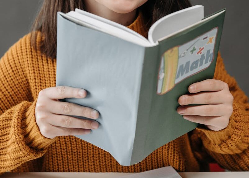 Teen girl smiling while holding a math book, showcasing her love for learning in a classroom setting.